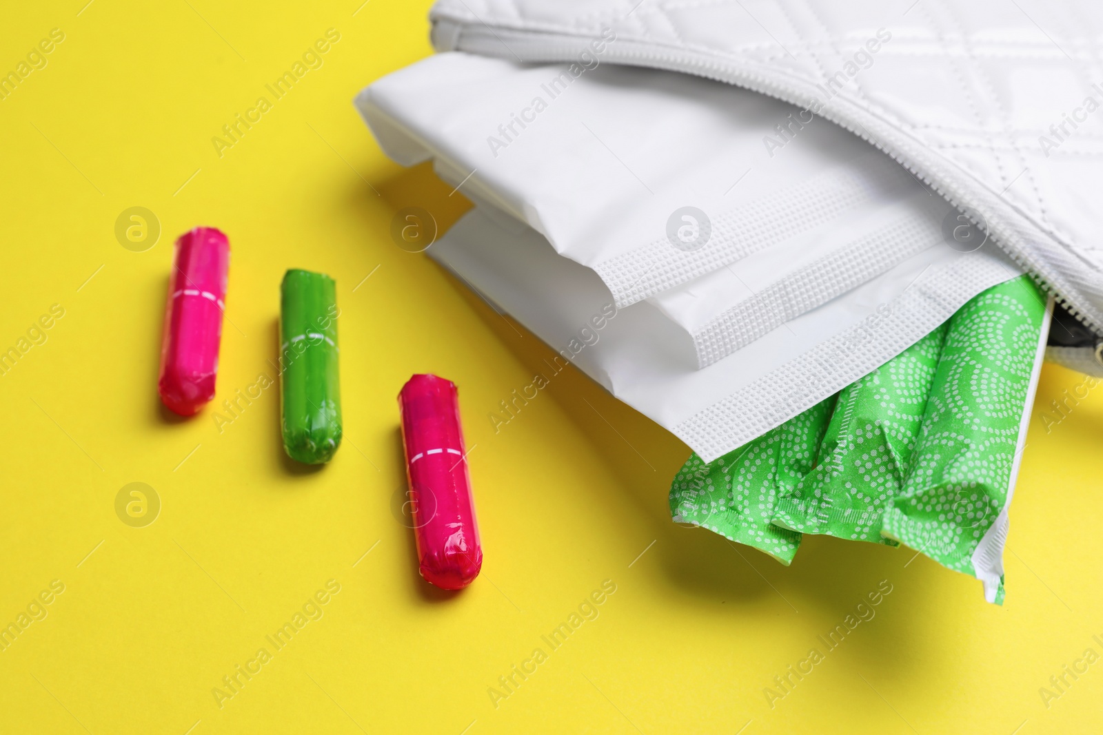 Photo of Bag with menstrual pads and tampons on yellow background, closeup