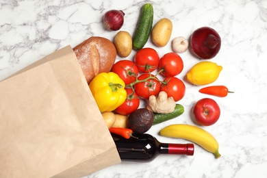 Photo of Shopping paper bag with different groceries on white marble background, flat lay