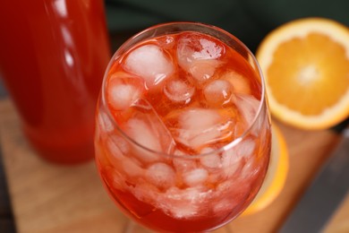 Aperol spritz cocktail and ice cubes in glass on wooden table, closeup