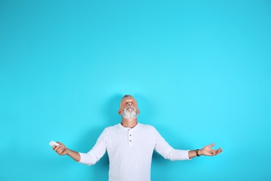 Photo of Senior man with air conditioner remote control on color background