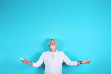 Senior man with air conditioner remote control on color background