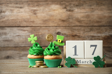 Photo of Decorated cupcakes, wooden block calendar and coins on table. St. Patrick's day celebration