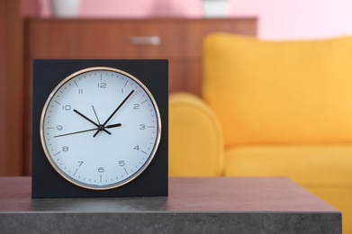 Photo of Stylish clock on table against blurred background. Time of day