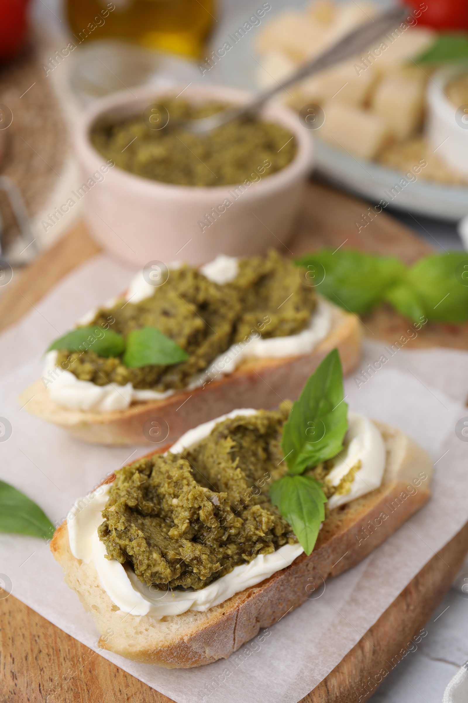 Photo of Tasty bruschettas with cream cheese, pesto sauce and fresh basil on wooden board, closeup