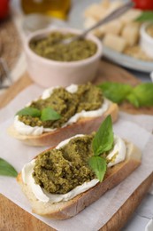 Tasty bruschettas with cream cheese, pesto sauce and fresh basil on wooden board, closeup