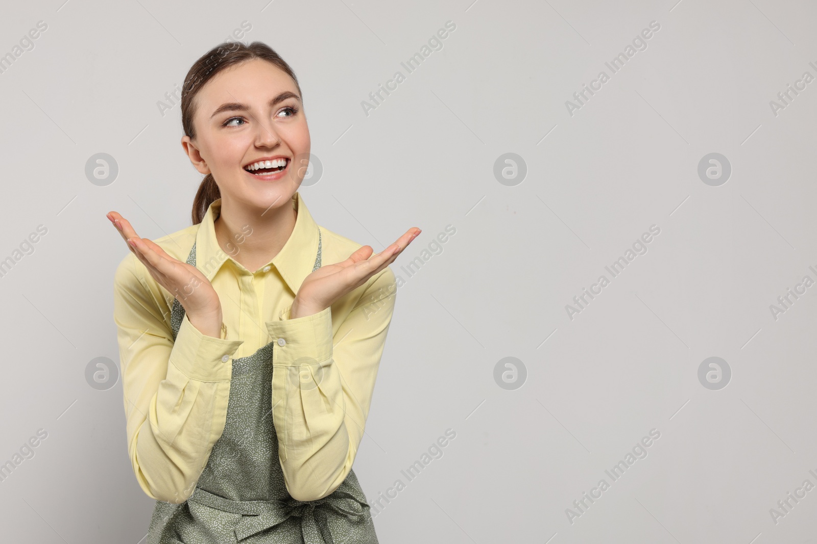 Photo of Beautiful young woman in clean apron with pattern on light grey background. Space for text