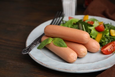 Photo of Delicious boiled sausages with salad on wooden table, closeup