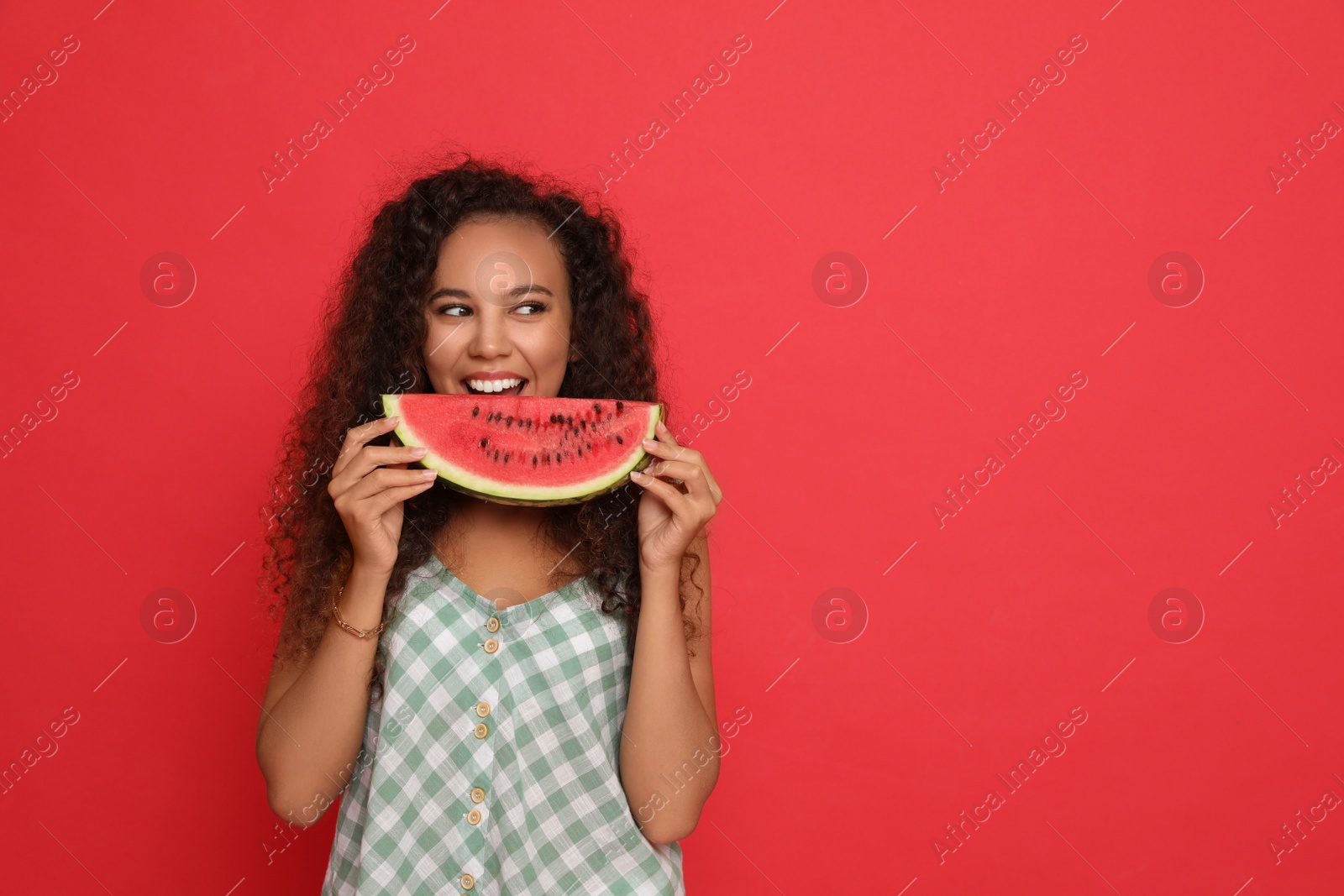 Photo of Beautiful young African American woman with slice of watermelon on red background. Space for text