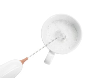 Photo of Whisking milk in cup with mini mixer (frother wand) isolated on white, top view