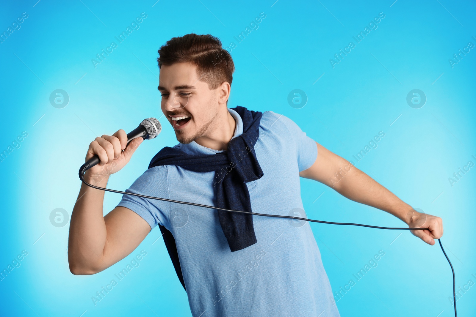 Photo of Young handsome man in casual clothes singing with microphone on color background