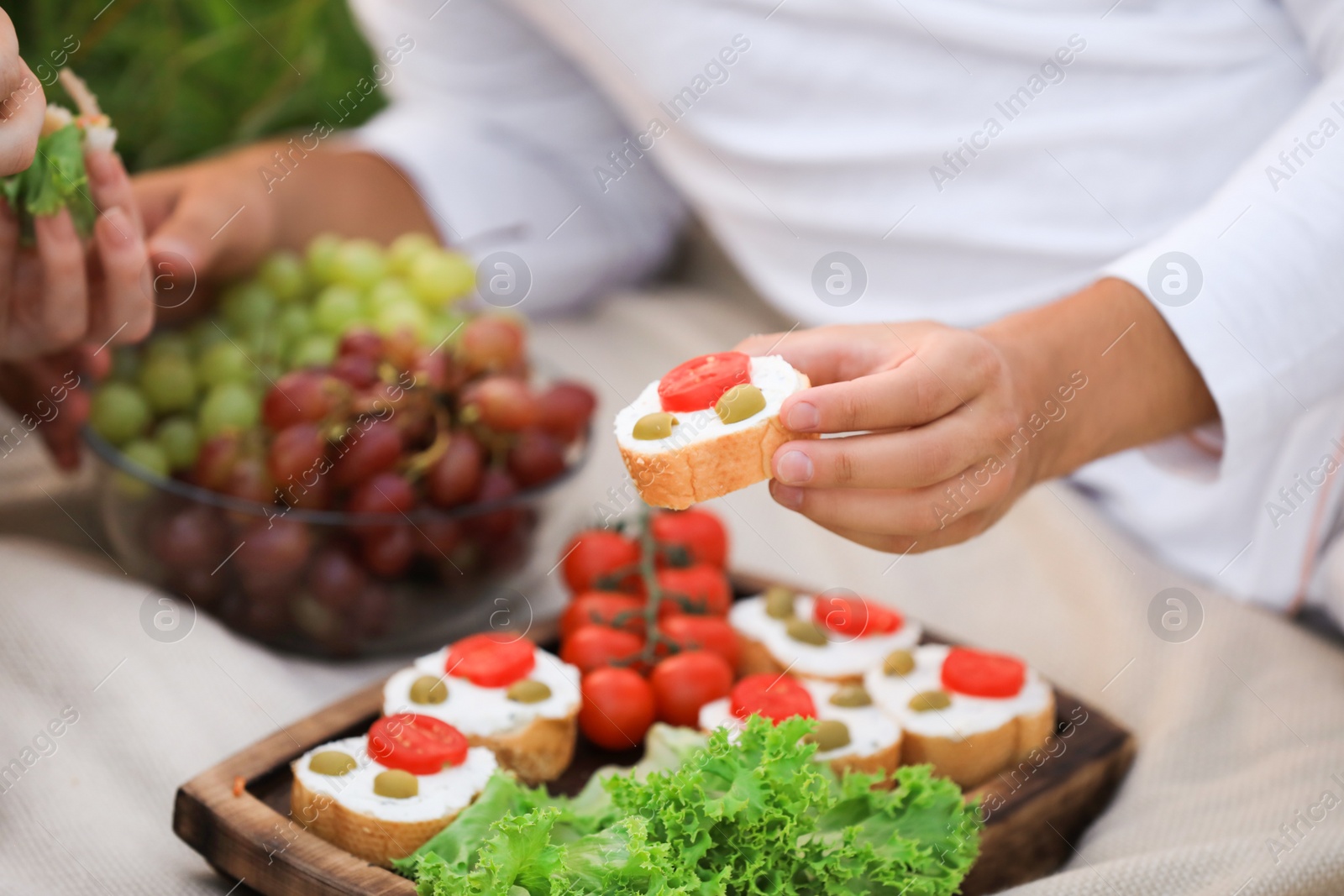 Photo of Young man with tasty sandwich and woman having picnic at park, closeup