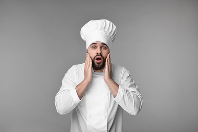 Photo of Surprised young chef in uniform on grey background