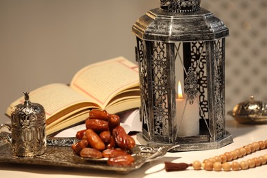 Photo of Arabic lantern, Quran, misbaha and dates on white table