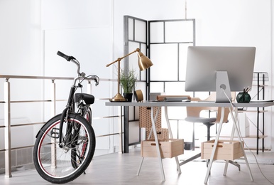 Stylish office interior with comfortable workplace and bicycle