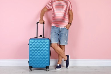 Photo of Man with suitcase near color wall. Vacation travel