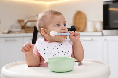 Cute little baby eating food in high chair at kitchen