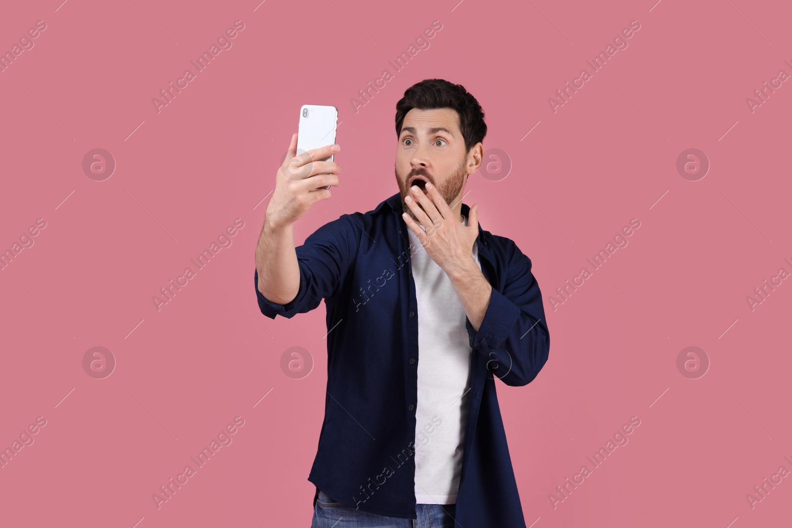 Photo of Surprised man taking selfie with smartphone on pink background