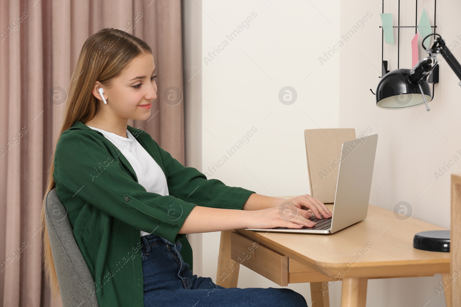 Photo of Teenage girl working on laptop at wooden desk in room