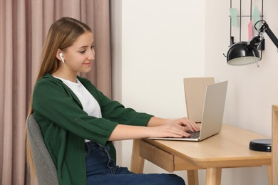 Photo of Teenage girl working on laptop at wooden desk in room