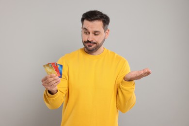 Photo of Confused man with credit cards on grey background. Debt problem