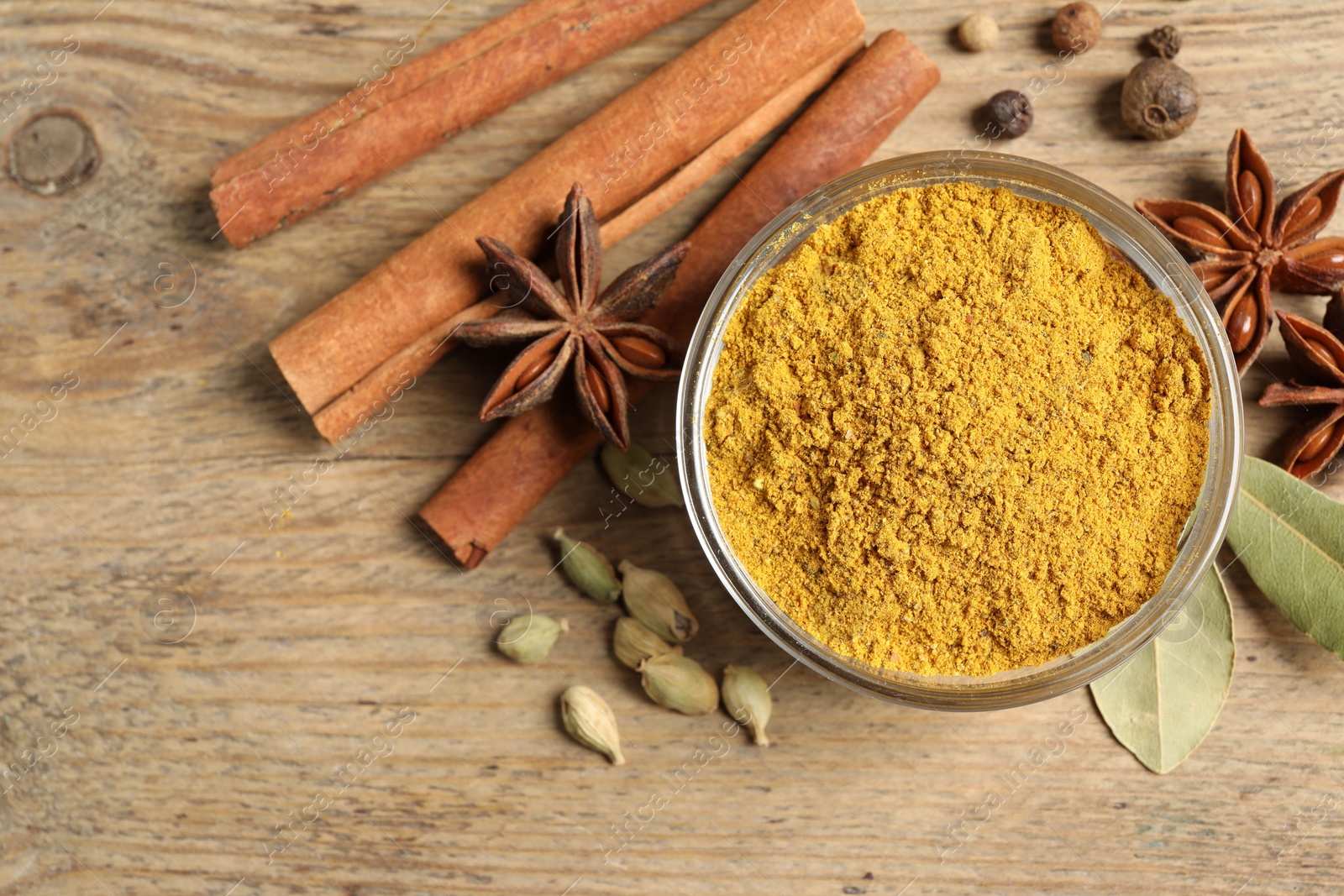 Photo of Curry powder in bowl and other spices on wooden table, flat lay. Space for text