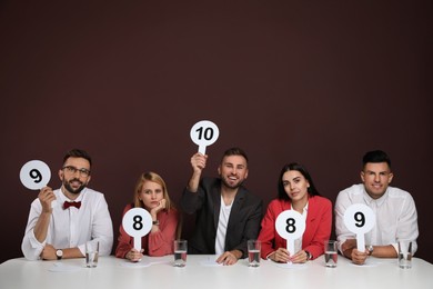 Photo of Panel of judges holding different score signs at table on brown background