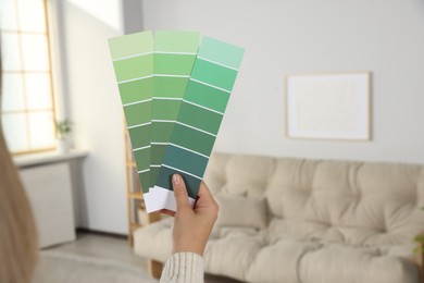 Photo of Woman with paint chips choosing color for wall in room, closeup. Interior design