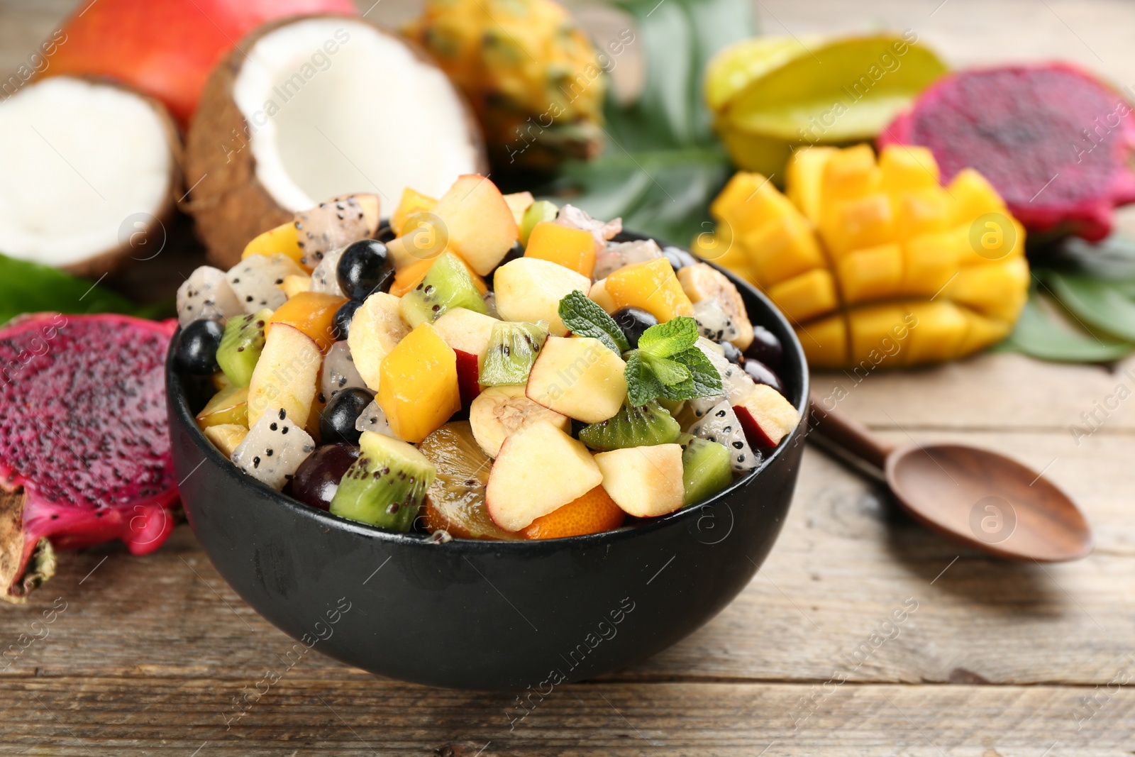 Photo of Delicious exotic fruit salad and ingredients on wooden table