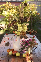 Photo of Composition with beautiful flowers, dry sunflowers and apples on wooden table outdoors. Autumn atmosphere