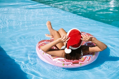 Young woman wearing Santa Claus hat on inflatable ring in swimming pool. Christmas vacation