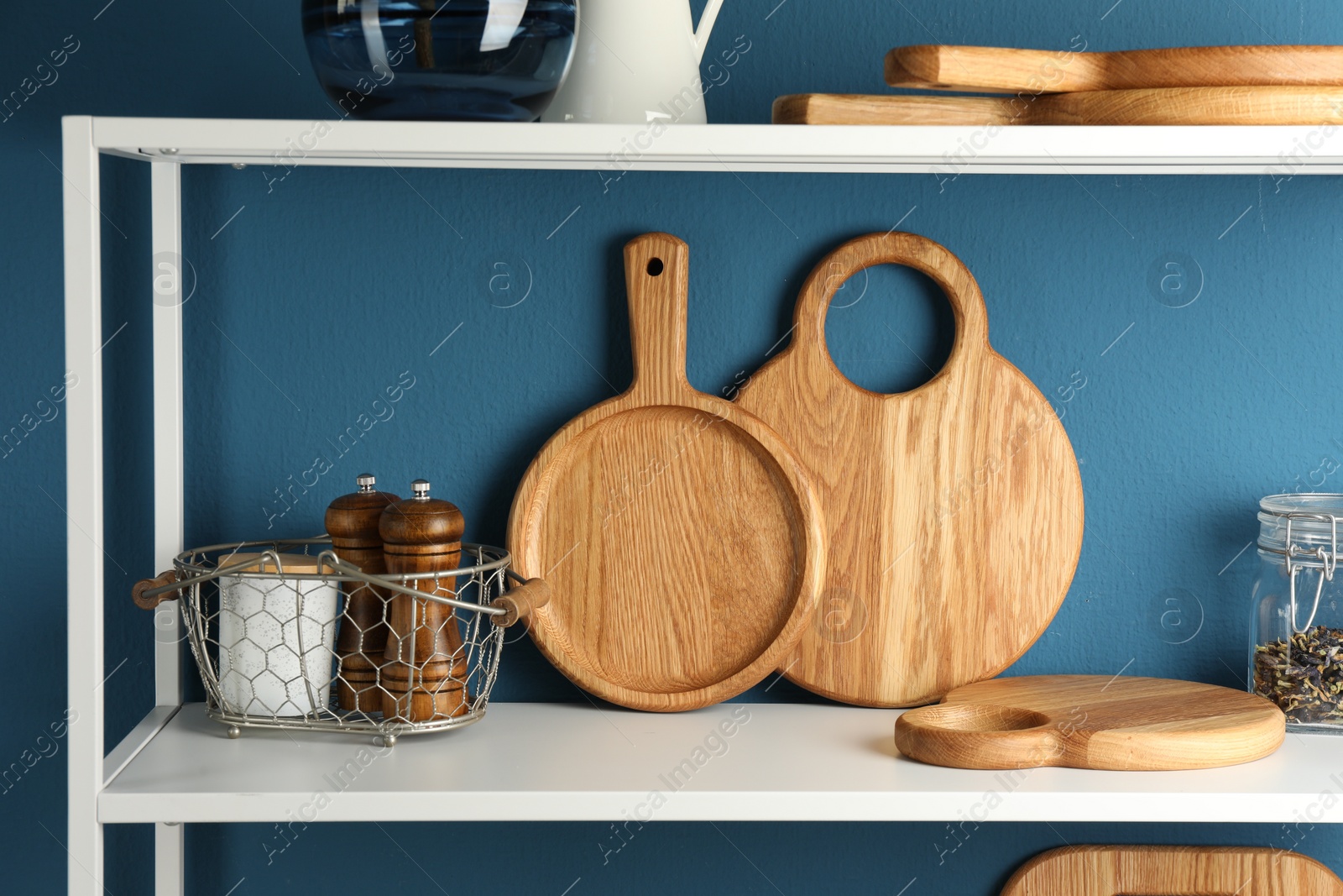 Photo of Wooden cutting boards, kitchen utensils and dry tea on shelving unit near blue wall