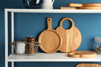 Photo of Wooden cutting boards, kitchen utensils and dry tea on shelving unit near blue wall