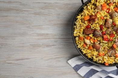 Delicious pilaf with meat, carrot and chili pepper served on wooden table, flat lay. Space for text