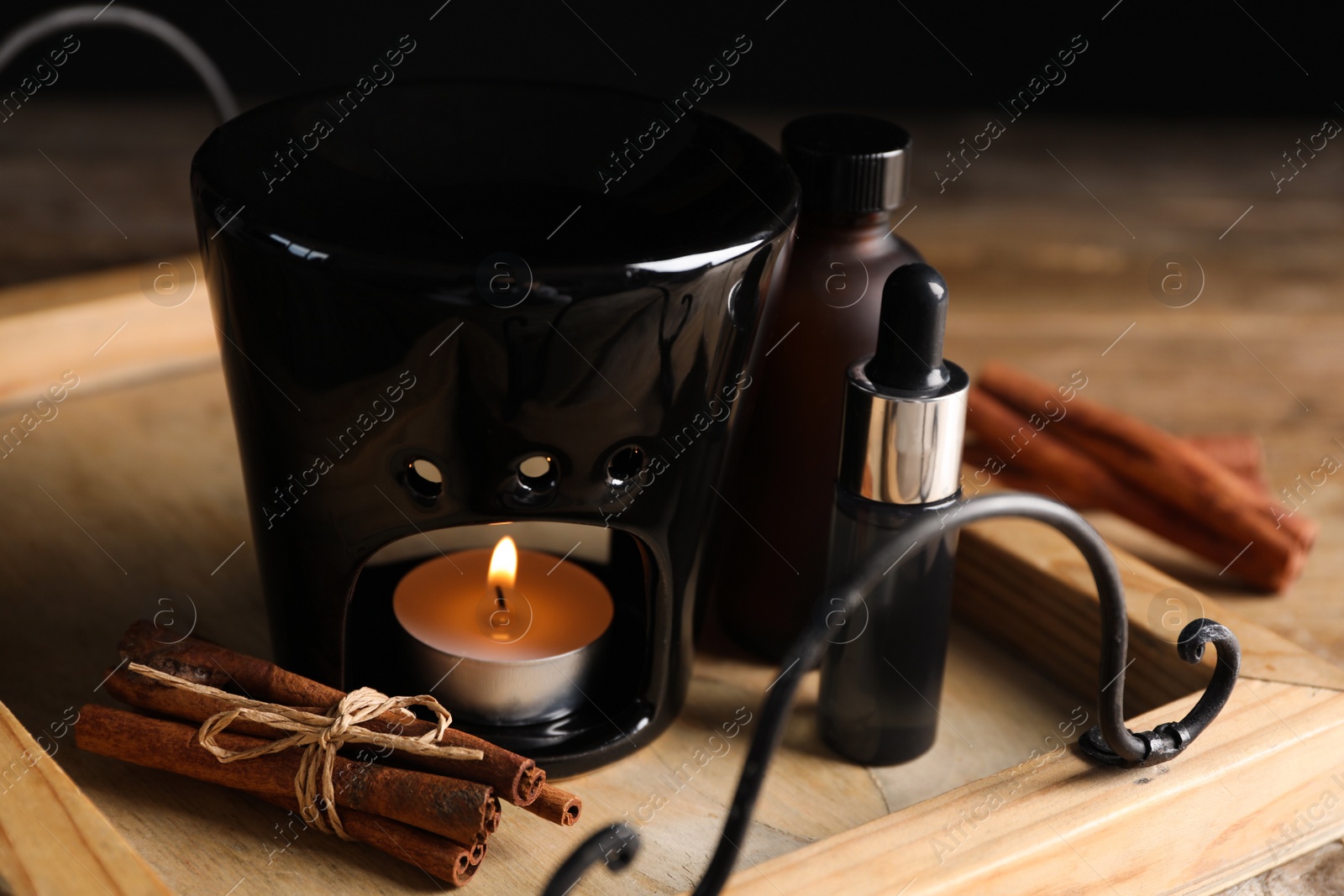 Photo of Aroma lamp and cinnamon essential oil on wooden tray