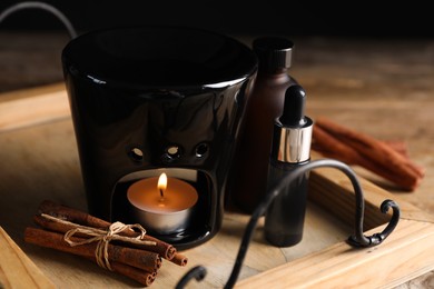 Photo of Aroma lamp and cinnamon essential oil on wooden tray