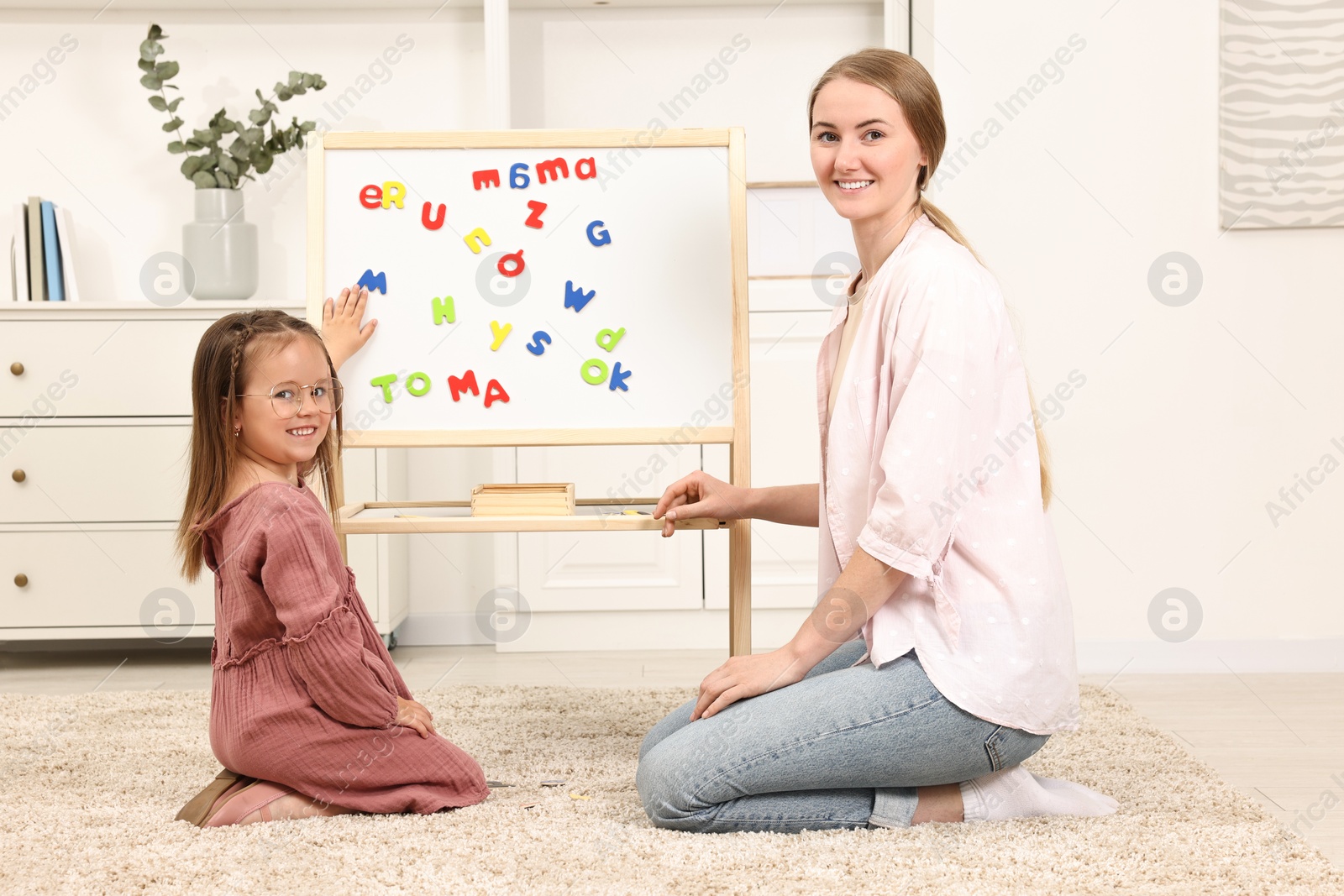 Photo of Mom teaching her daughter alphabet with magnetic letters at home