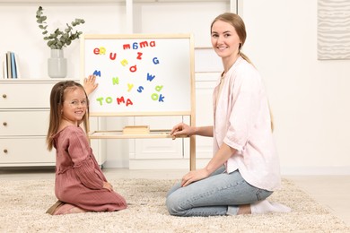 Photo of Mom teaching her daughter alphabet with magnetic letters at home