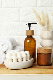 Photo of Different bath accessories, personal care products and spikelets in vase on white table near brick wall