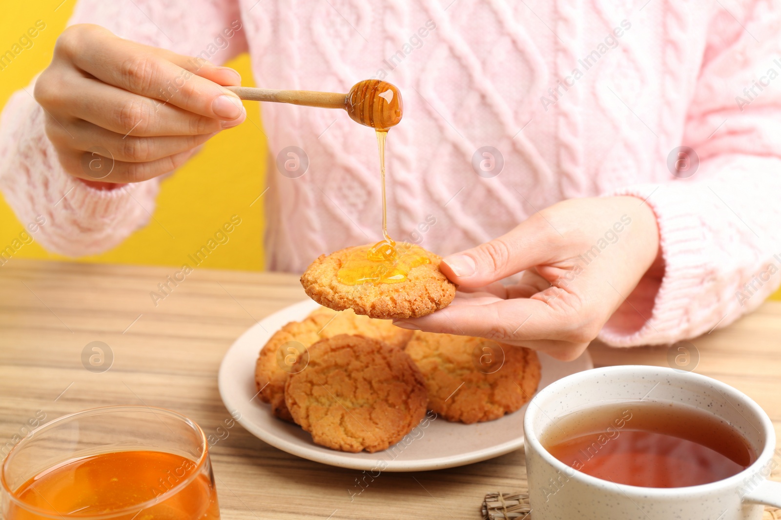 Photo of Woman pouring honey onto cookie at wooden table, closeup