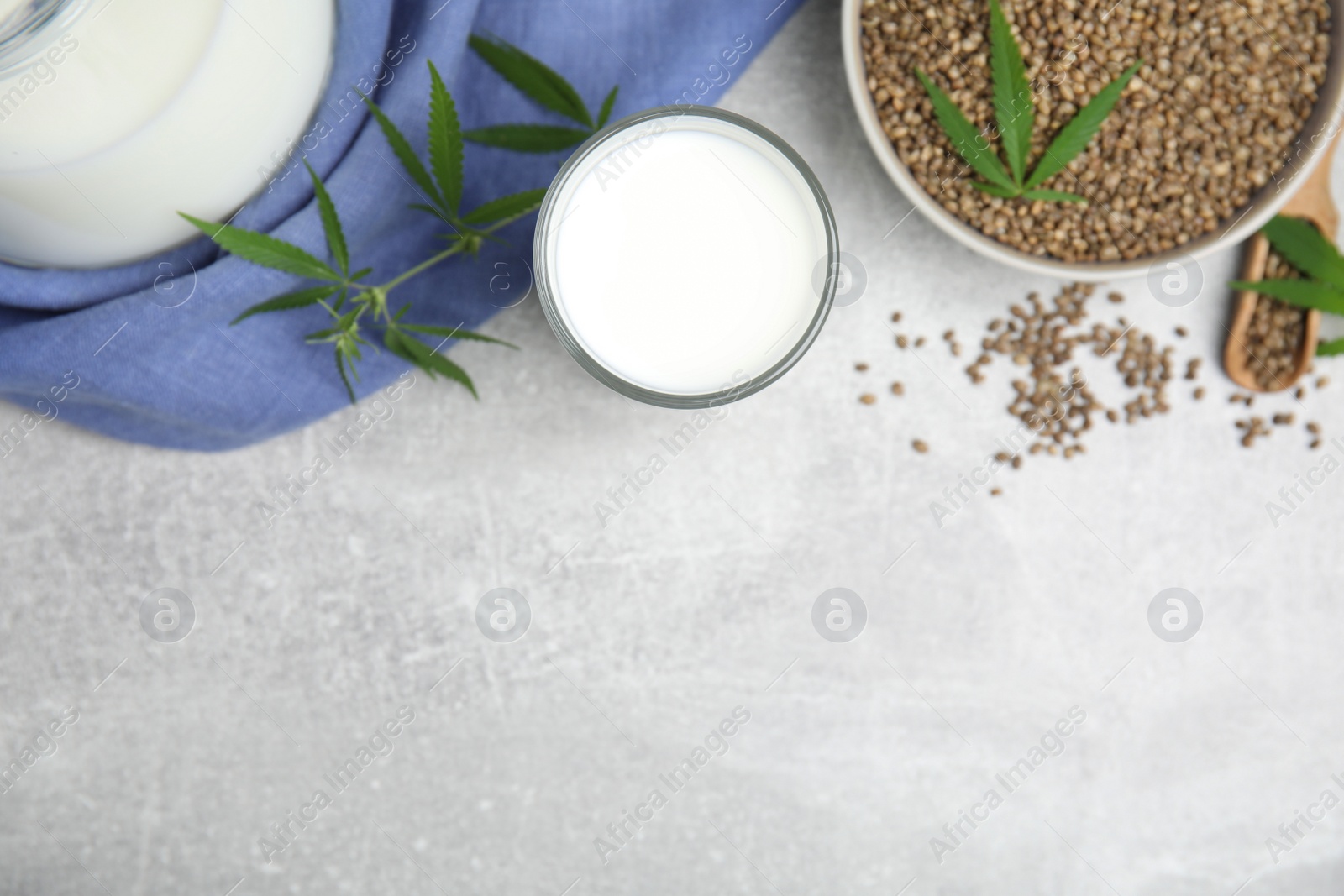 Photo of Hemp milk and seeds with fresh leaves on light grey table, flat lay. Space for text