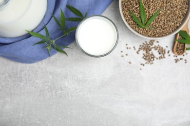 Hemp milk and seeds with fresh leaves on light grey table, flat lay. Space for text