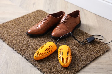 Photo of Pair of stylish shoes with modern electric footwear dryer on door mat indoors