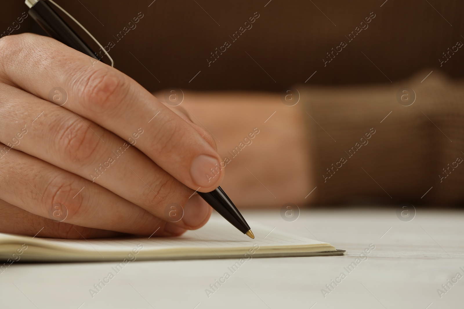 Photo of Man writing in notebook at white table, closeup. Space for text