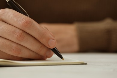 Photo of Man writing in notebook at white table, closeup. Space for text
