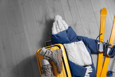 Suitcase with warm clothes and skis on wooden floor, flat lay. Winter vacation