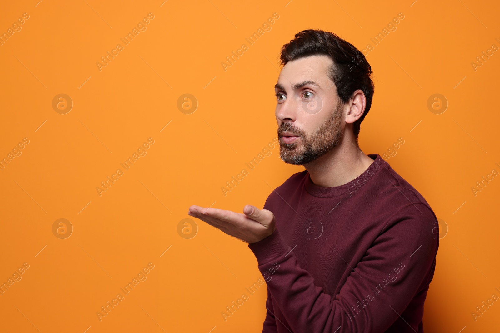 Photo of Handsome man blowing kiss on orange background. Space for text