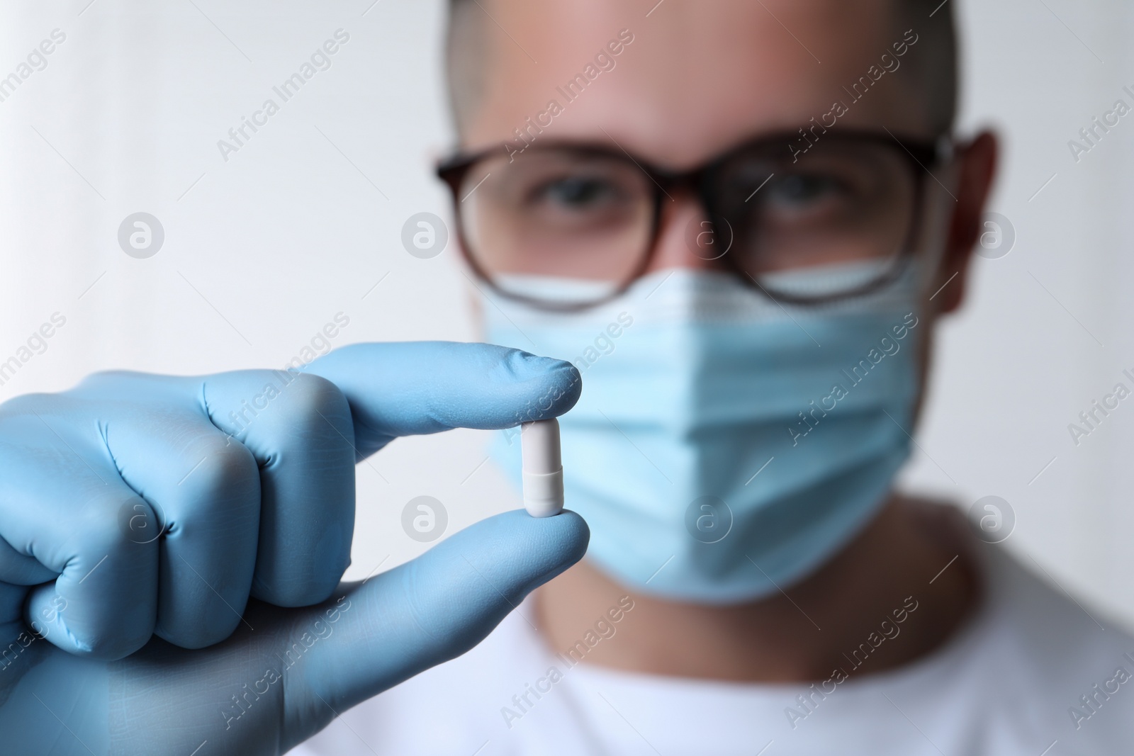 Photo of Doctor holding pill on light background, selective focus. Space for text