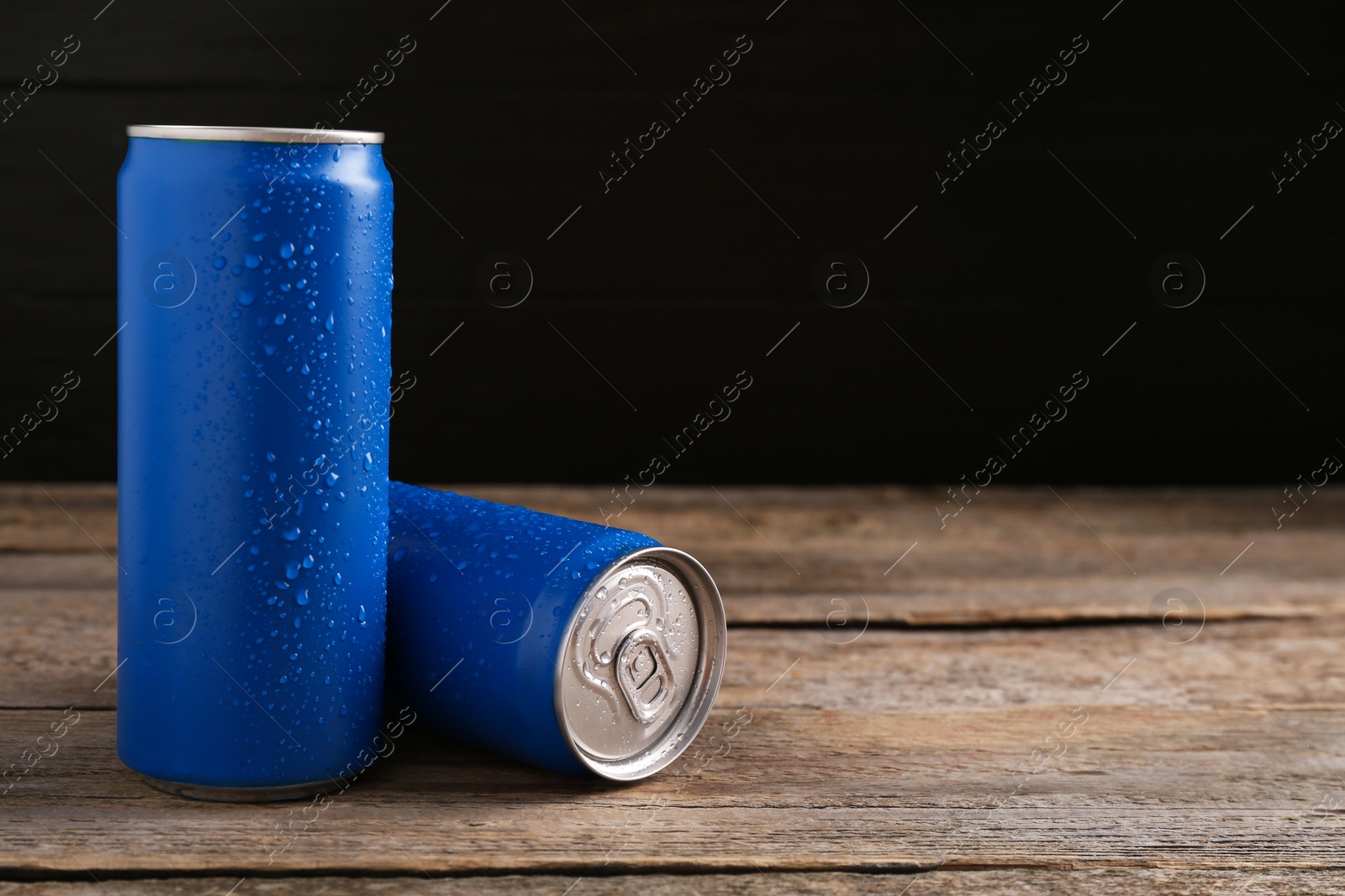 Photo of Energy drinks in wet cans on wooden table, space for text