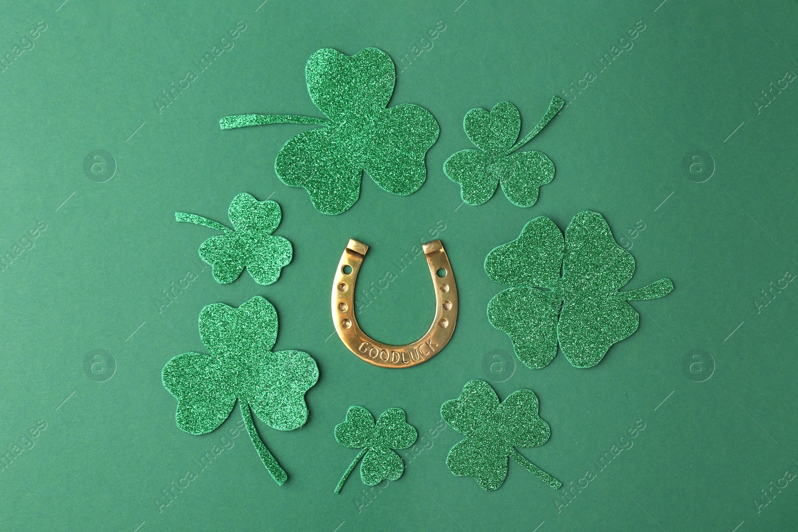 Photo of St. Patrick's day. Golden horseshoe and decorative clover leaves on green background, flat lay