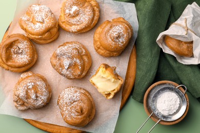 Photo of Delicious profiteroles filled with cream on green background, flat lay